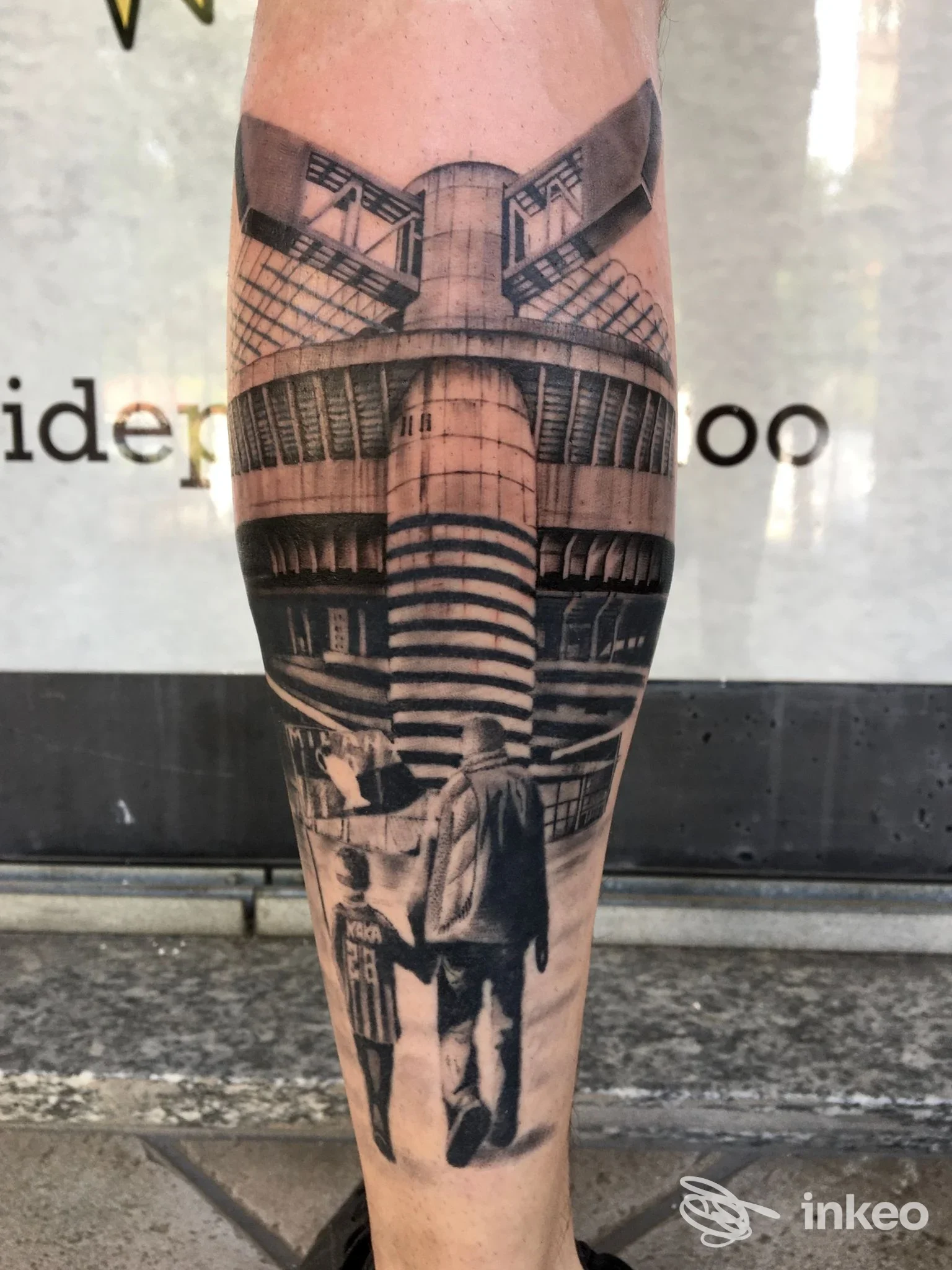 Tattoo realistico in tonalità di grigio su polpaccio raffigurante architettura urbana con edifici e una scena con figure, senza aggiunte testuali o elementi promozionali, visibile chiaramente sulla pelle.