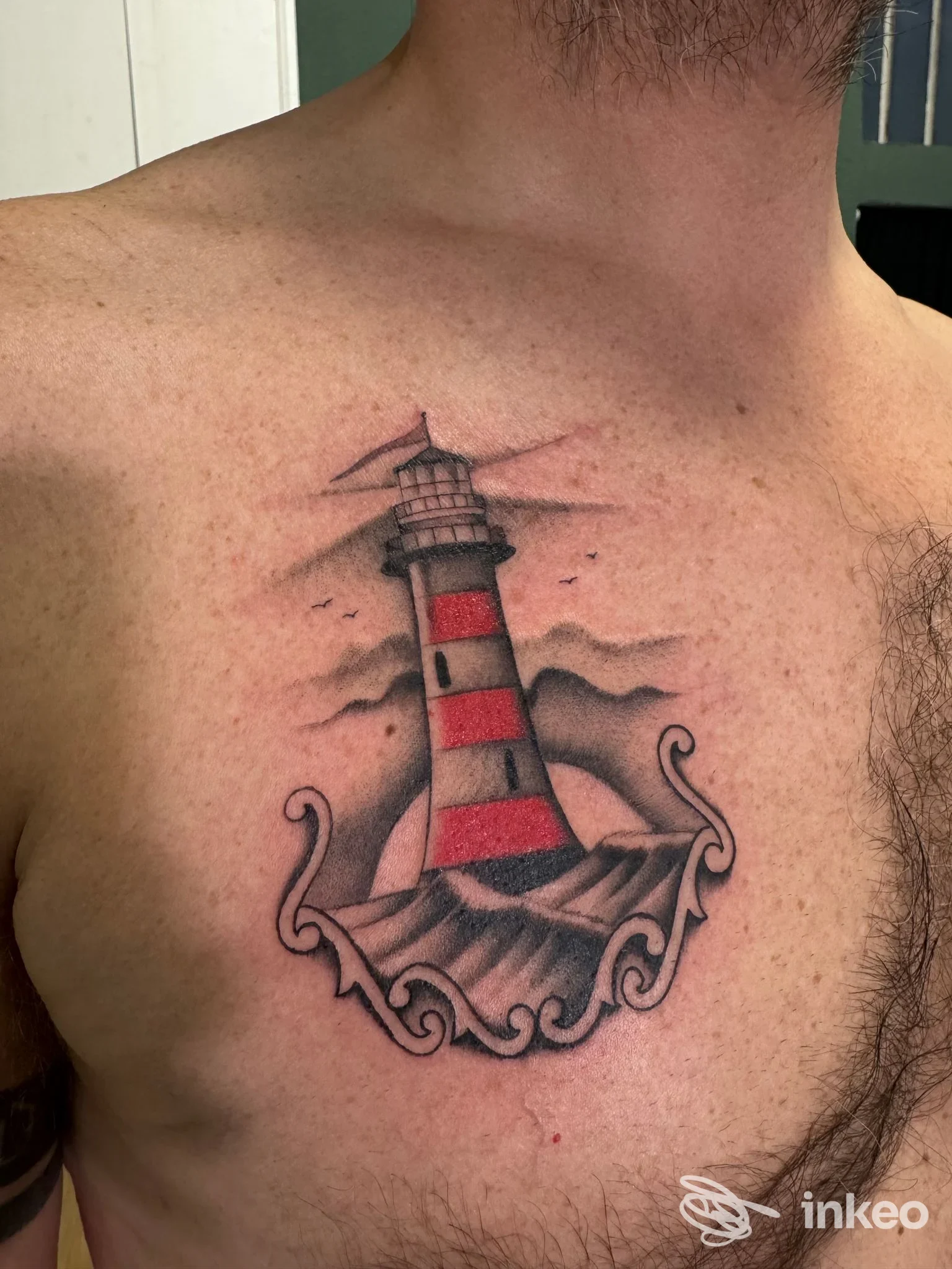 Tattoo su torace di un faro a fasce rosso e grigie tra onde, realizzata sulla pelle. nessun volto visibile, nessun overlay.