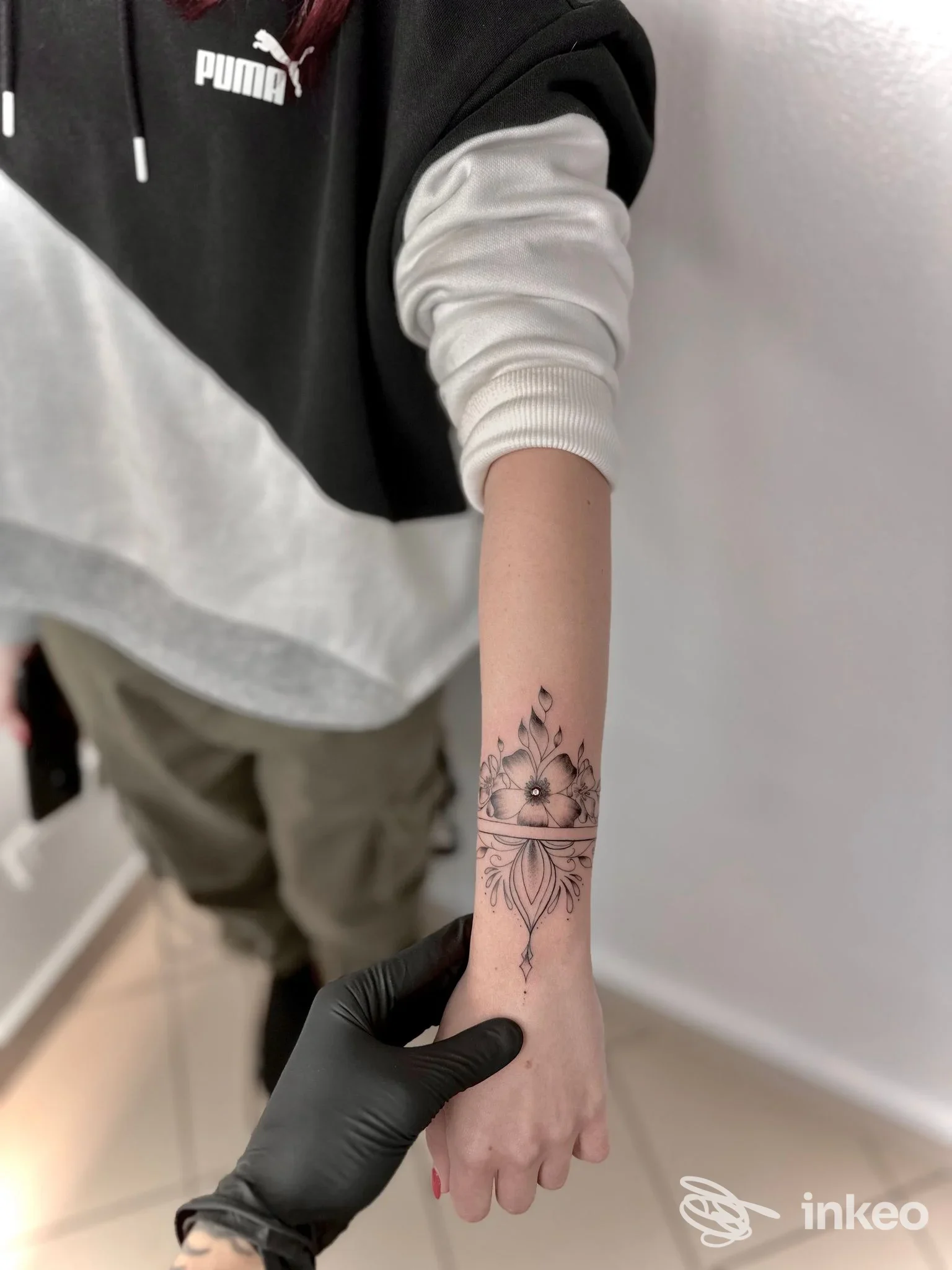 Braccio sinistro di una persona con un tatuaggio floreale sull’avambraccio, tatuaggio visibile in primo piano; scatto realizzato in uno studio, Falcos Tattoo Studio.