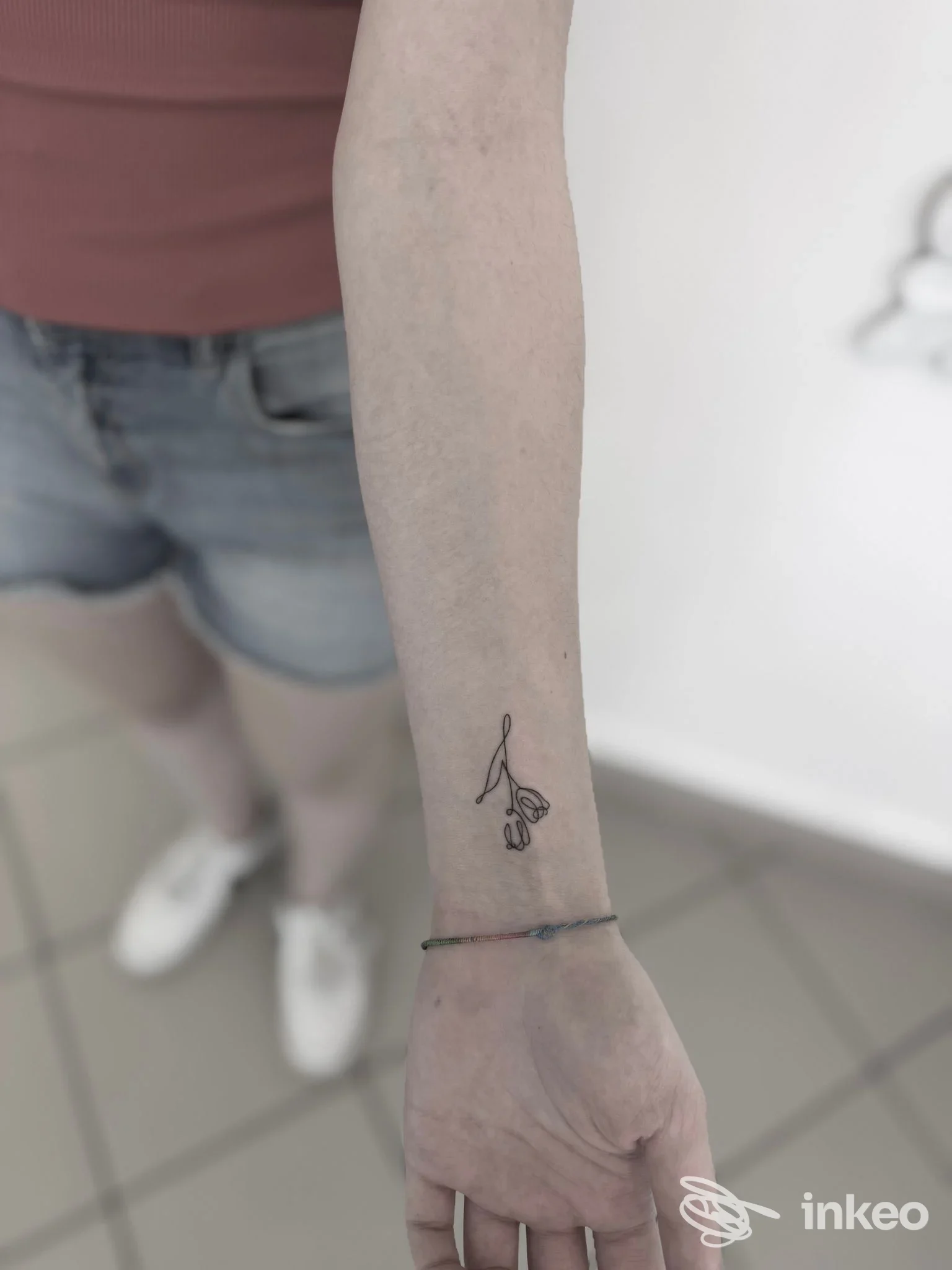 Tattoo piccolo e stilizzato di una mano sull'avambraccio, senza volto visibile, sfondo neutro, braccio esposto e braccialetto sottile.