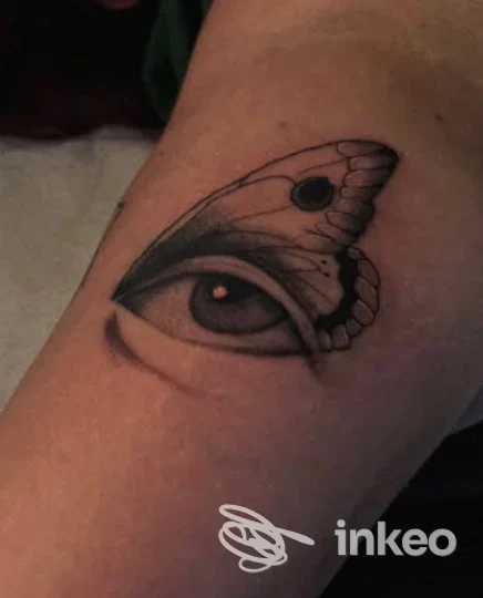 Tatuaggio visibile su pelle, raffigurante un occhio con un'ala di farfalla: linee nette in bianco e nero su brasato sulla pelle.