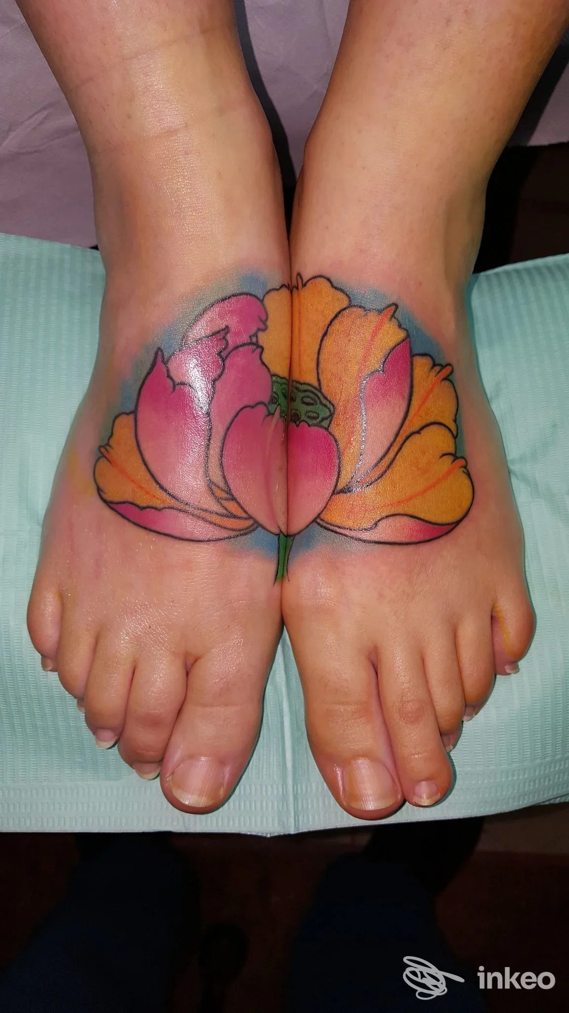 Due piedi con un grande tattoo floreale colorato sulle superfici dorsali, visibile su entrambe le dita e l’area superiore dei piedi, scatto singolo.
