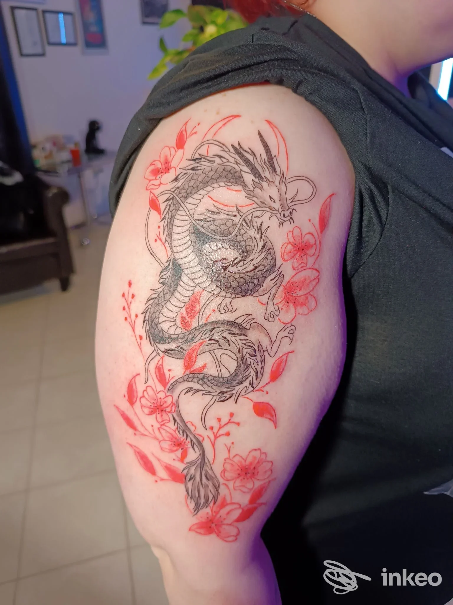 Tattoo sul braccio superiore raffigurante un drago circondato da fiori rossi, realizzato sulla pelle della persona.