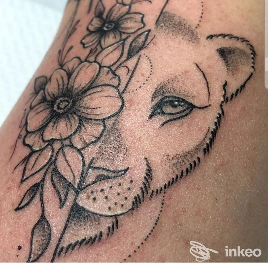Tattoo su pelle sull'avambraccio: ritratto stilizzato con fiori, esecuzione a linework nera.