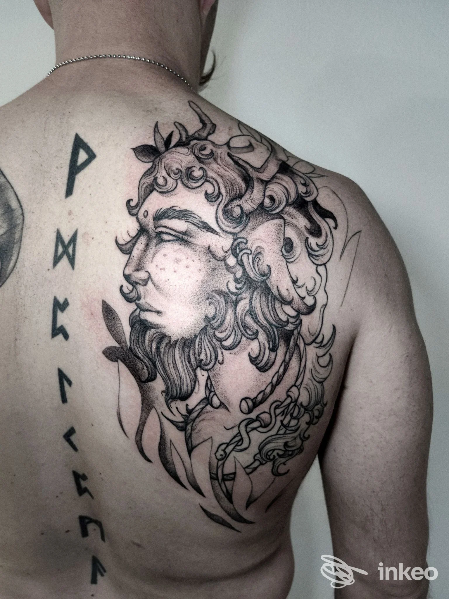 Tattoo sul dorso di una persona: ritratto classico con capelli ondulati e decorazioni vegetali, visibile sulla spalla sinistra.