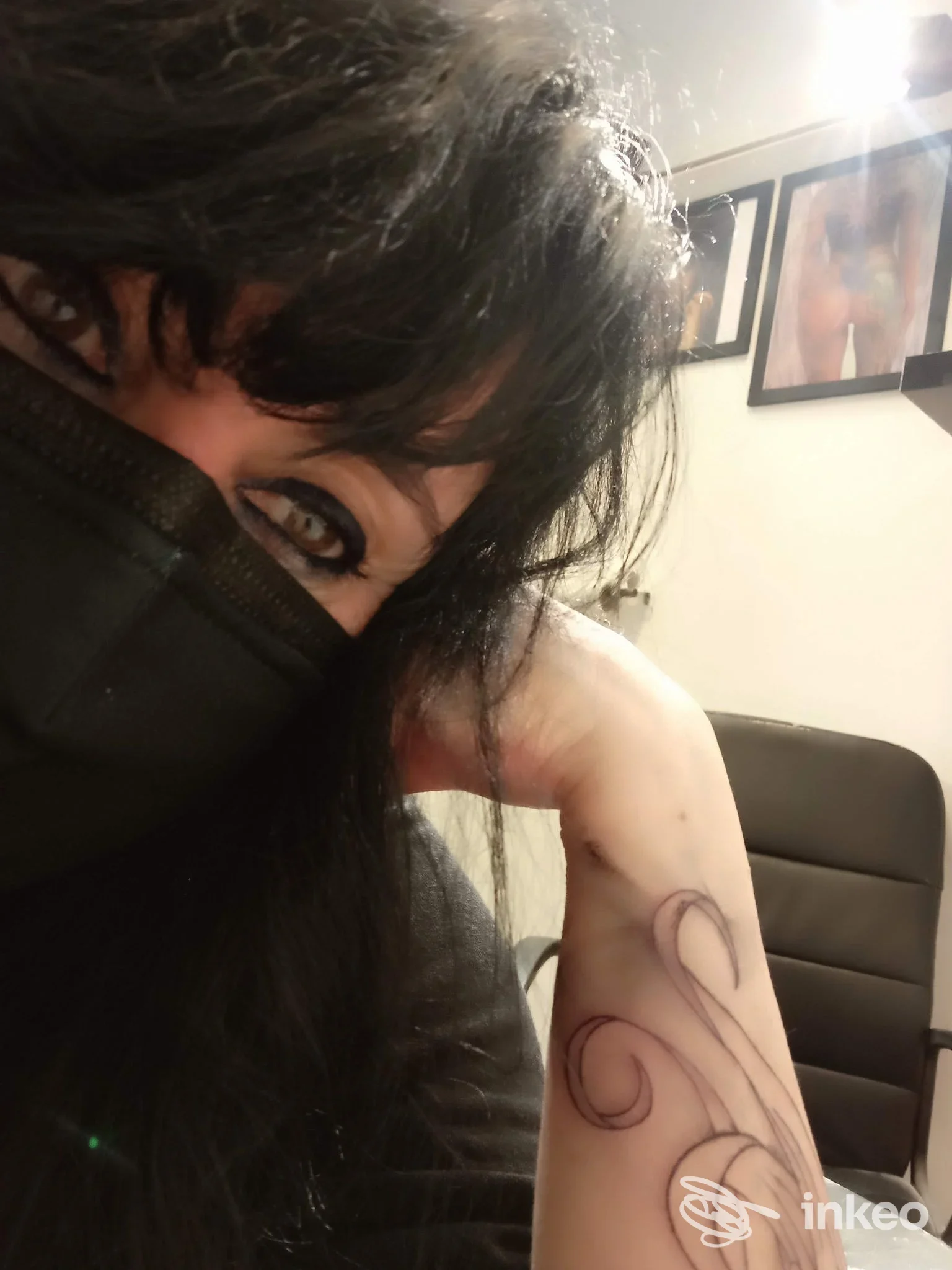Veduta parziale dell'avambraccio sinistro di una persona con disegno di tatuaggio a linee viola, visibile sopra la scrivania di uno studio; la persona porta una mascherina nera e si intravede il volto parziale.