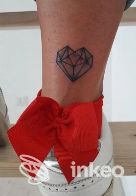 Tatuaggio geometrico a cuore eseguito sulla pelle della gamba, visibile vicino alla caviglia, in tinta nera.