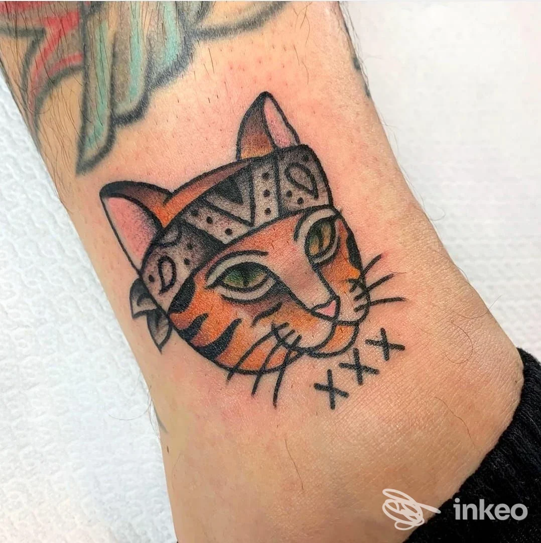 Tatuaggio su pelle raffigurante la testa di un gatto stile vintage, colorato con occhi verdi e baffi neri, situato sull’avambraccio o polpaccio. Nessun testo aggiunto o logo visibile.