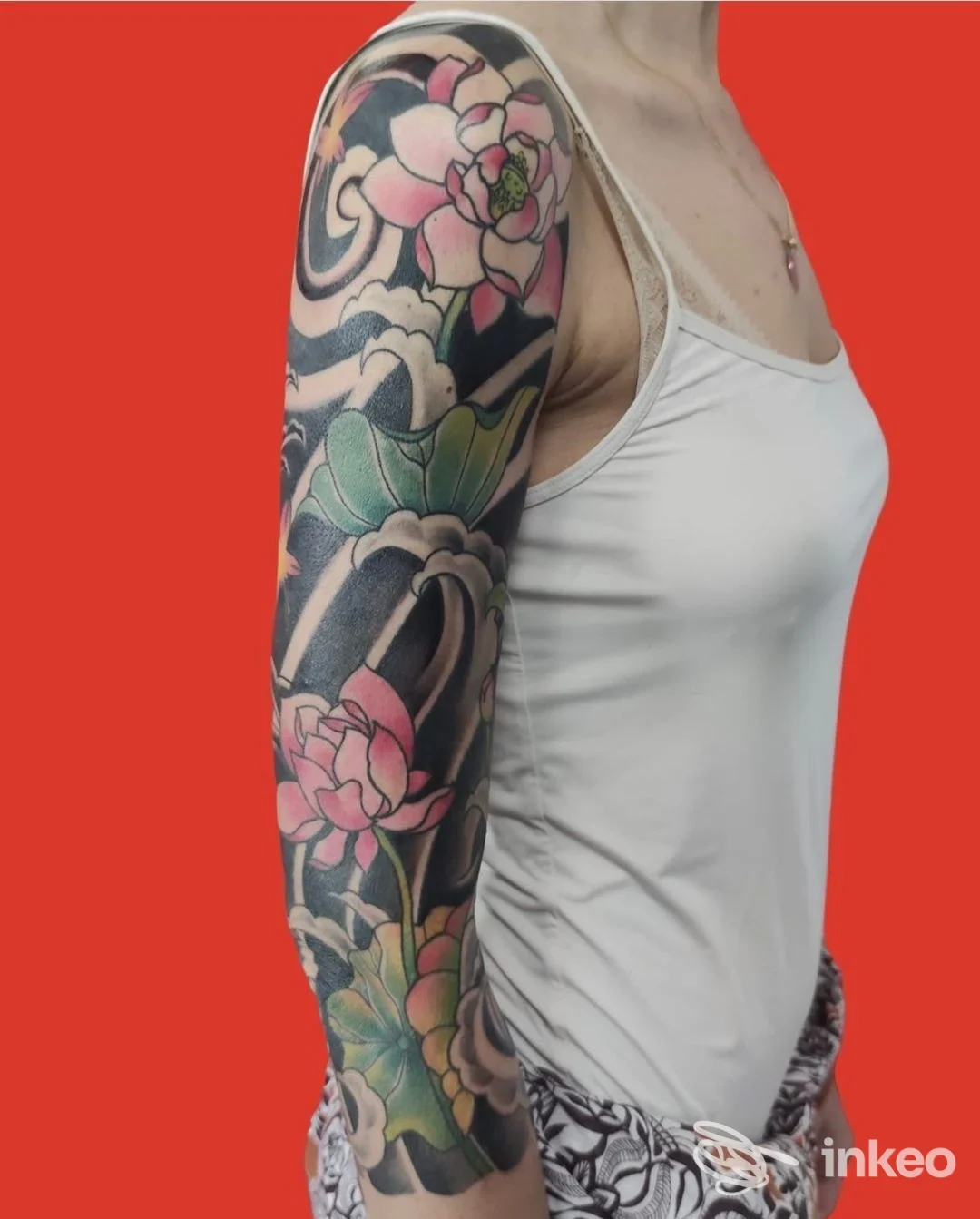 Braccio di una persona con tatto a manica colorata su pelle, indossa canotta bianca; sfondo rosso.