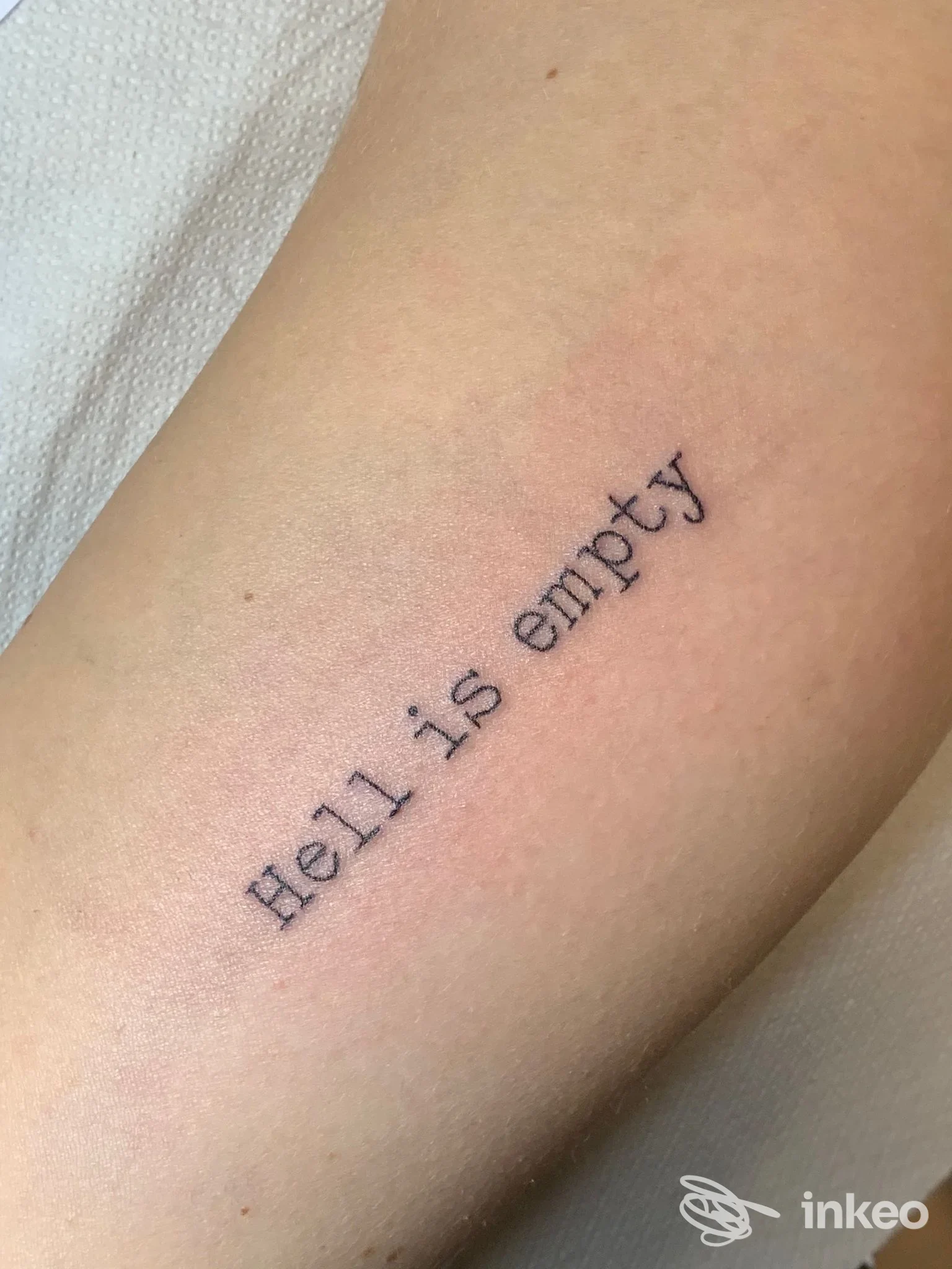Tattoo su avambraccio: una scritta nera diagonale che dice Hell is empty. nessun viso visibile. scritto su pelle reale, senza elementi di interfaccia o foto aggiunta.