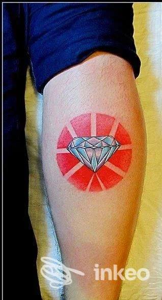 Cerchio rosso con raggi circonda un diamante azzurro: tatuaggio visibile sull'avambraccio.