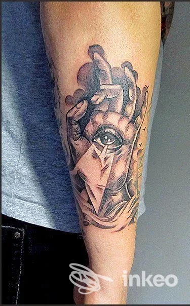 Tattoo sul braccio raffigurante un occhio realistico inserito in elementi astratti, tonalità scure, visibile parte dell’avambraccio.
