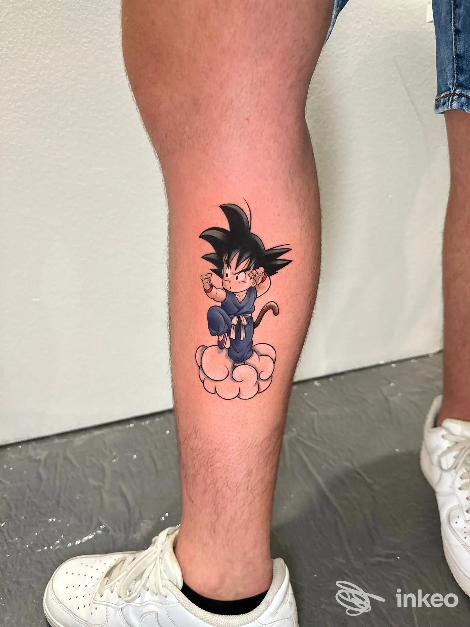 Tattoo su gamba raffigurante Goku su una nuvola, stile anime, colori predominanti nero e blu.