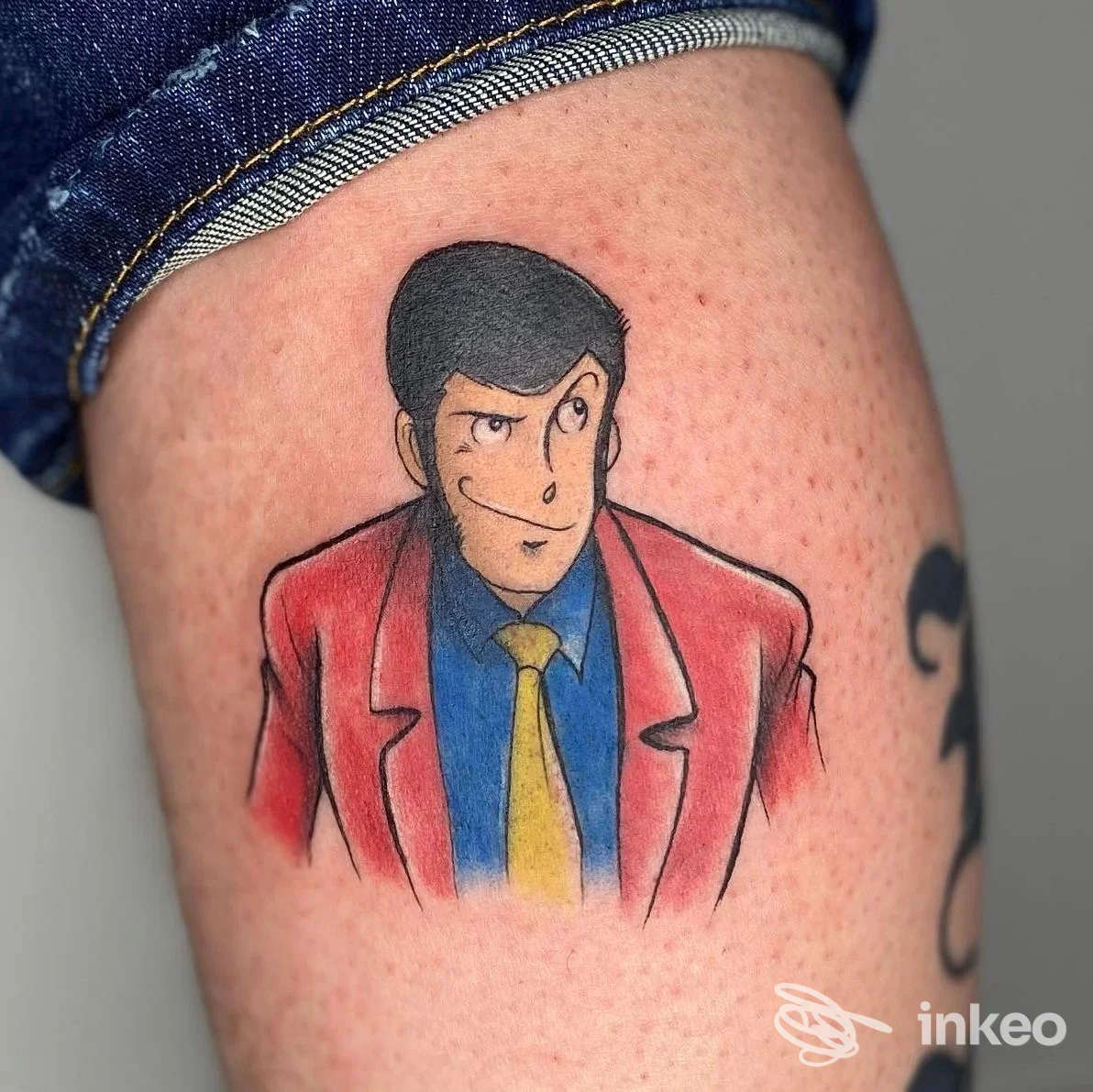 Tattoo su pelle di un braccio raffigurante una cartolina animata con una figura maschile in giacca rossa, camicia blu e cravatta gialla.