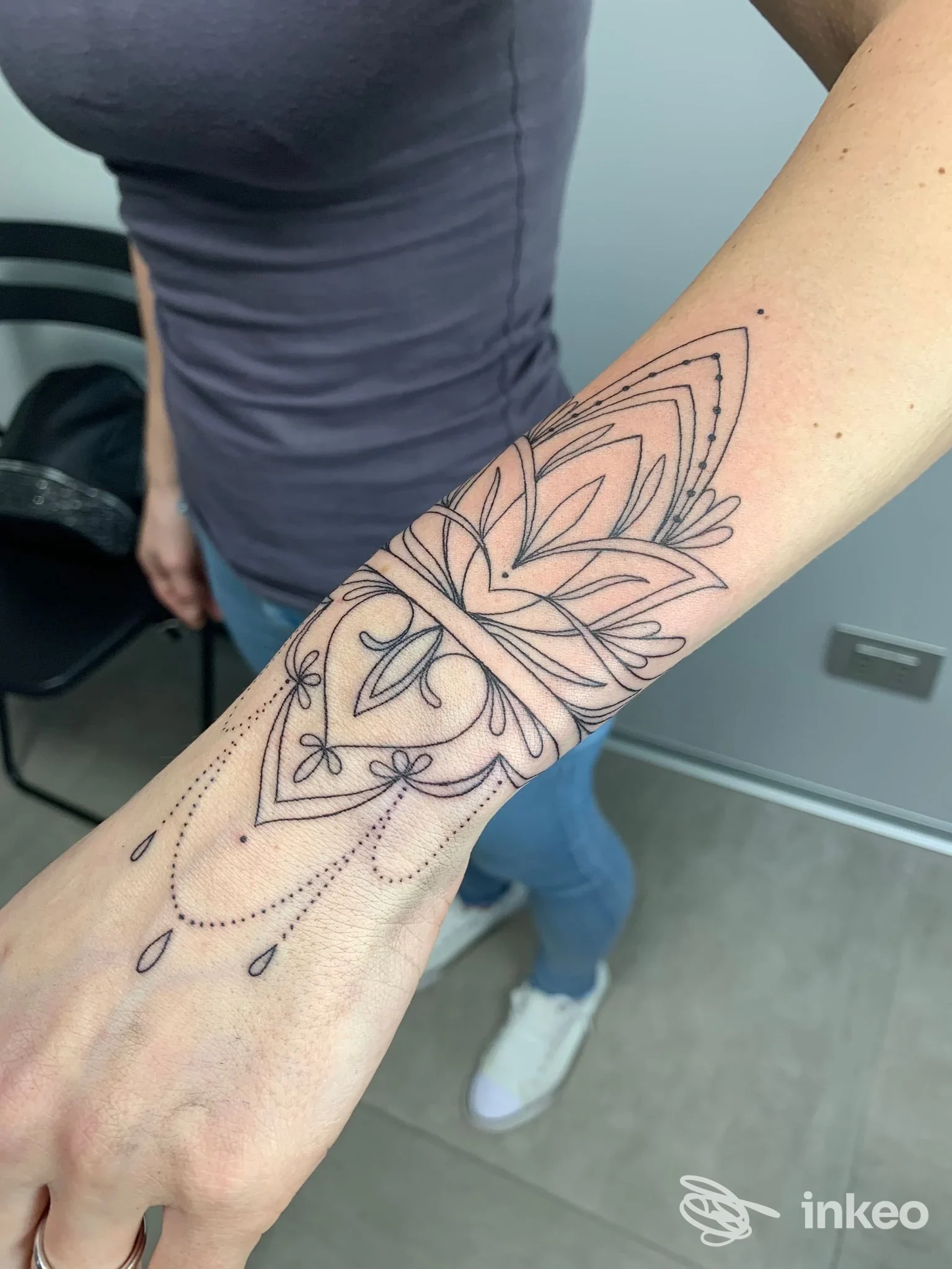Tattoo sulla pelle dell’avambraccio: disegno geometrico a fiori in stile linework, senza colore, visibile su braccio di una persona.