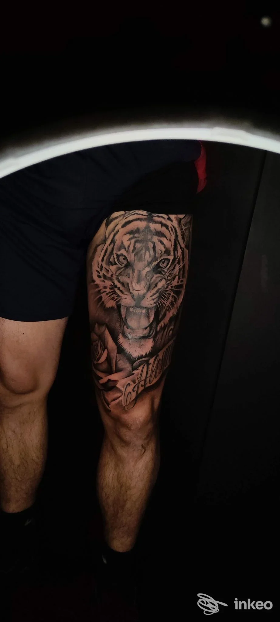 Tattoo realistico di tigre visibile sulla coscia di una persona, con dettagli e linee nette, sfondo scuro.
