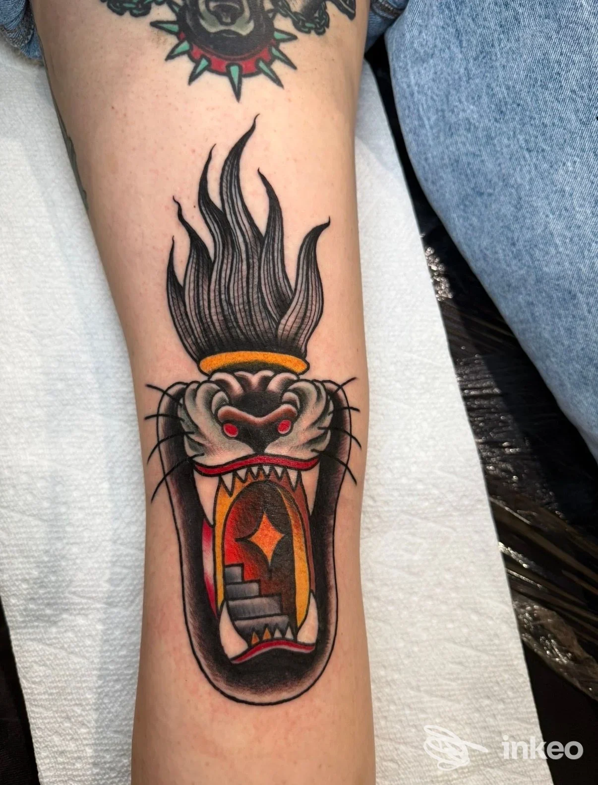 Tattoo su avambraccio raffigurante una creatura aperta in bocca, colori nero, rosso e arancione.