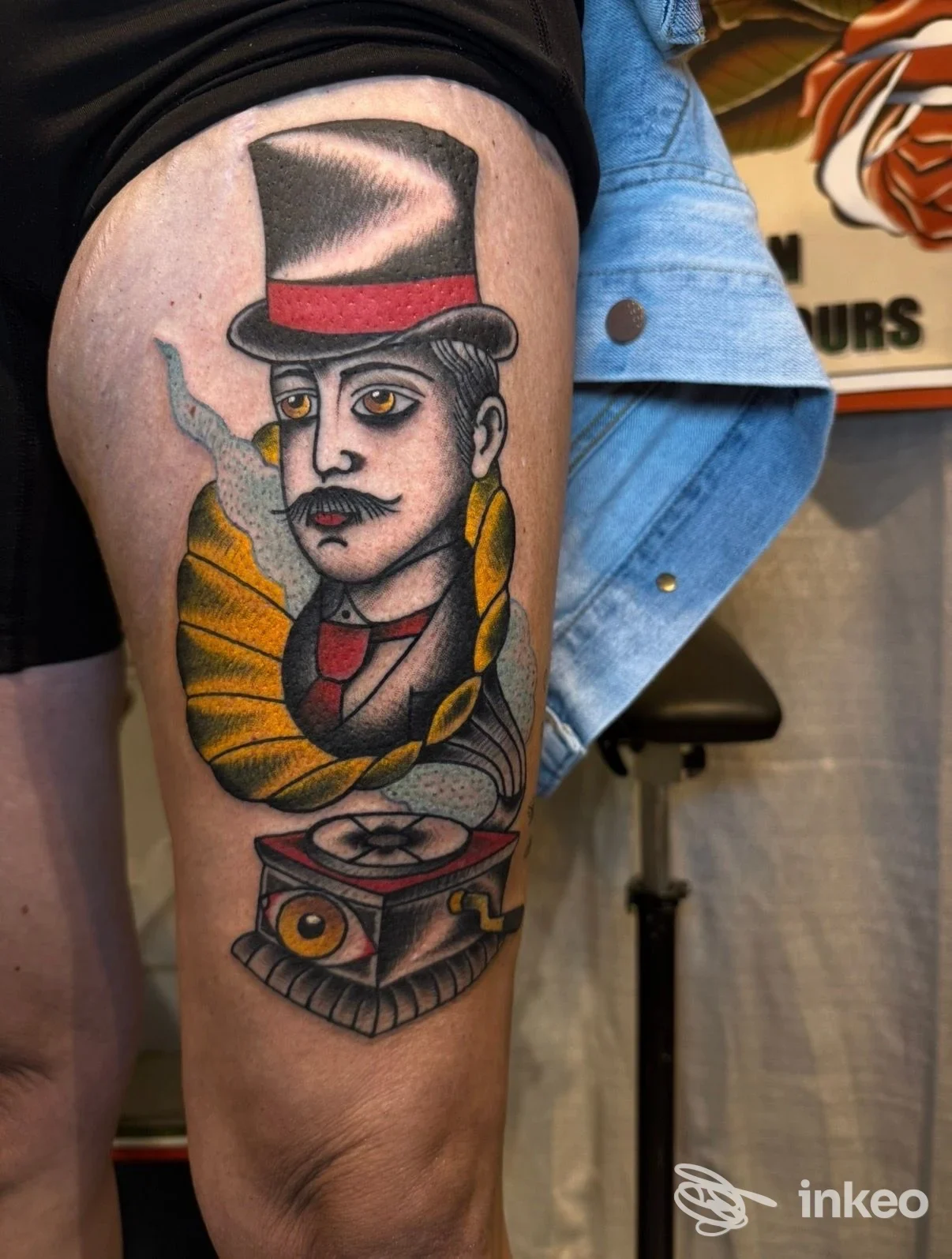 Tattoo tradizionale su pelle umana: ritratto di un uomo con cappello nero e fascia rossa, sul braccio superiore, accompagnato da elementi colorati.