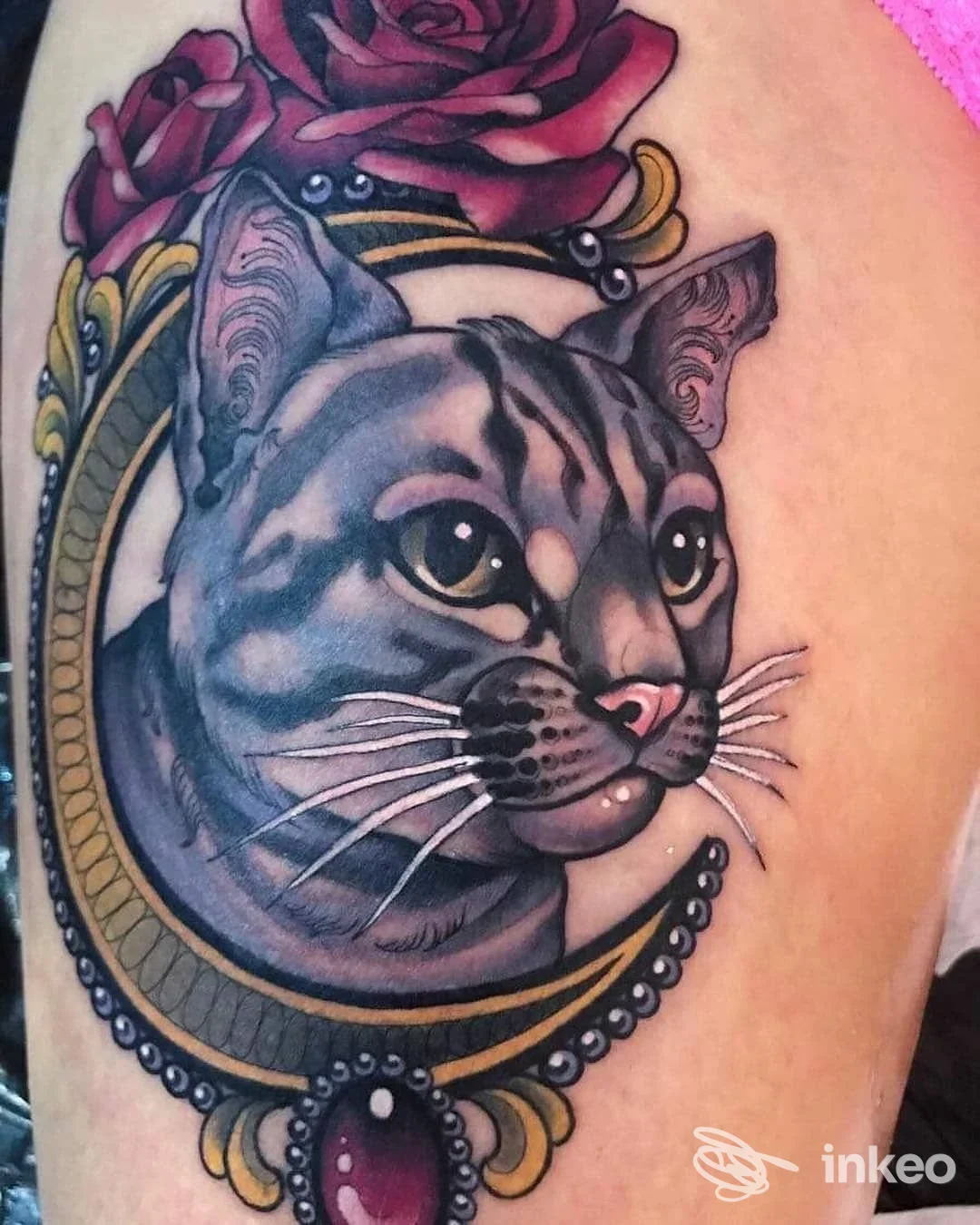 Tattoo realistico di gatto grigio con ornamenti dorati e rose rosa sul braccio sinistro.
