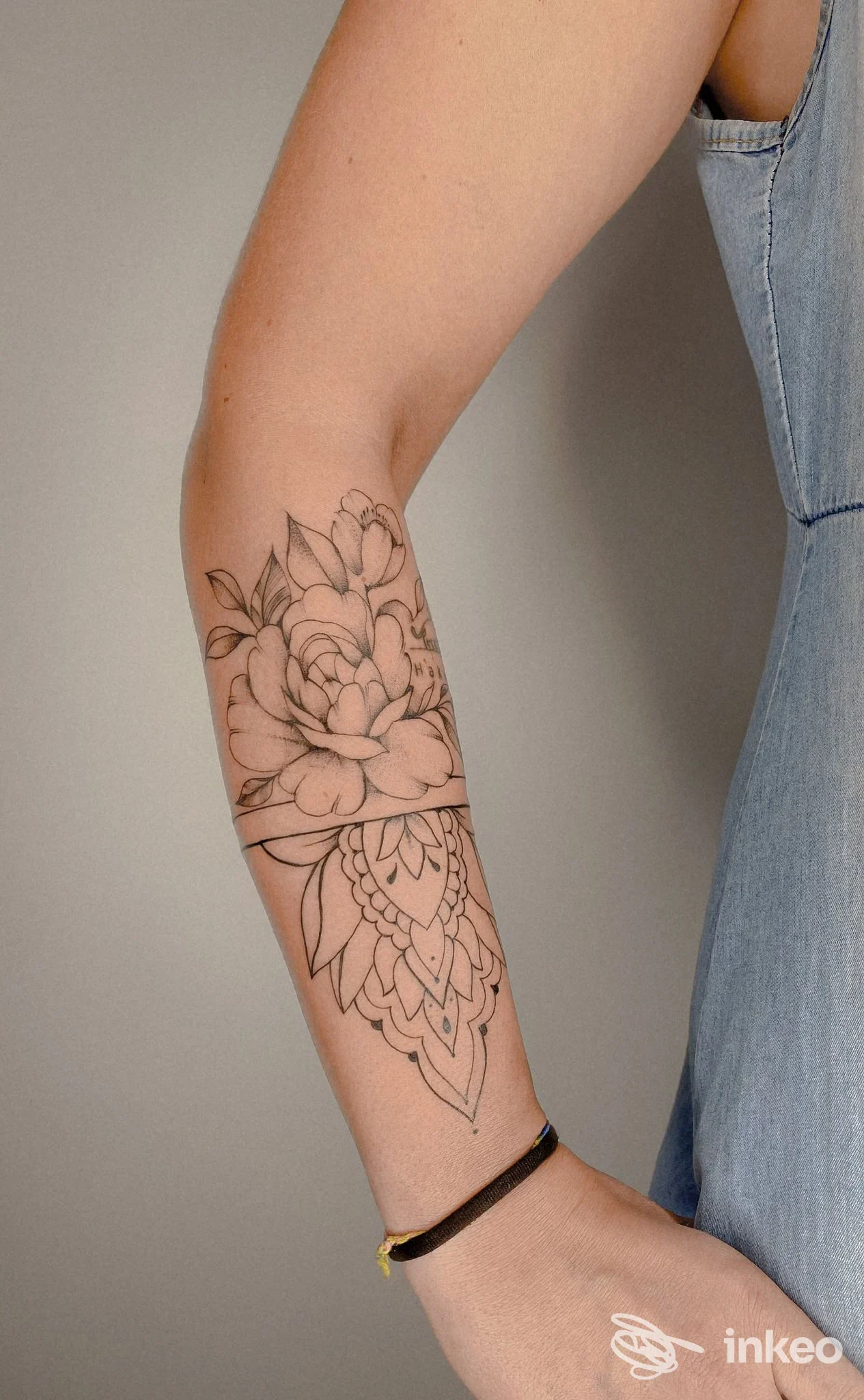 Tattoo floreale su braccio, linea nera su pelle, visibile da avambraccio a polso, con braccialetto nero, indossando una maglietta o cardigan. Studio inattivo.