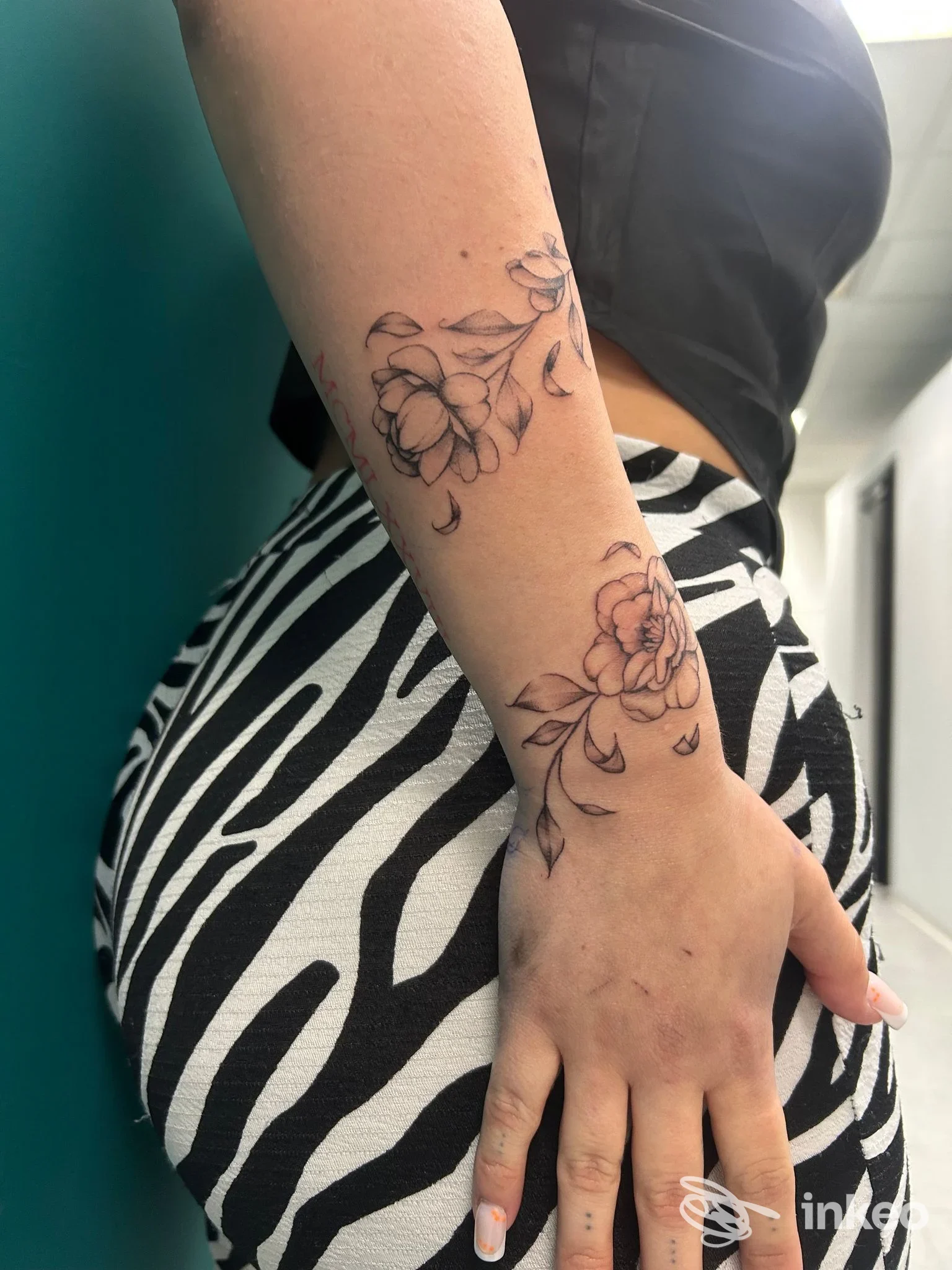 Tattoo floreale su pelle visibile sull'avambraccio di una persona, sequenza di braccio e mano in primo piano, senza volto.