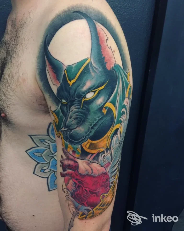 Tattoo colorato su braccio raffigurante una creatura simile a un drago con corna, con dettagli vivaci e sfondo scuro; sul lato sinistro si intravede un motivo a fiore azzurro.