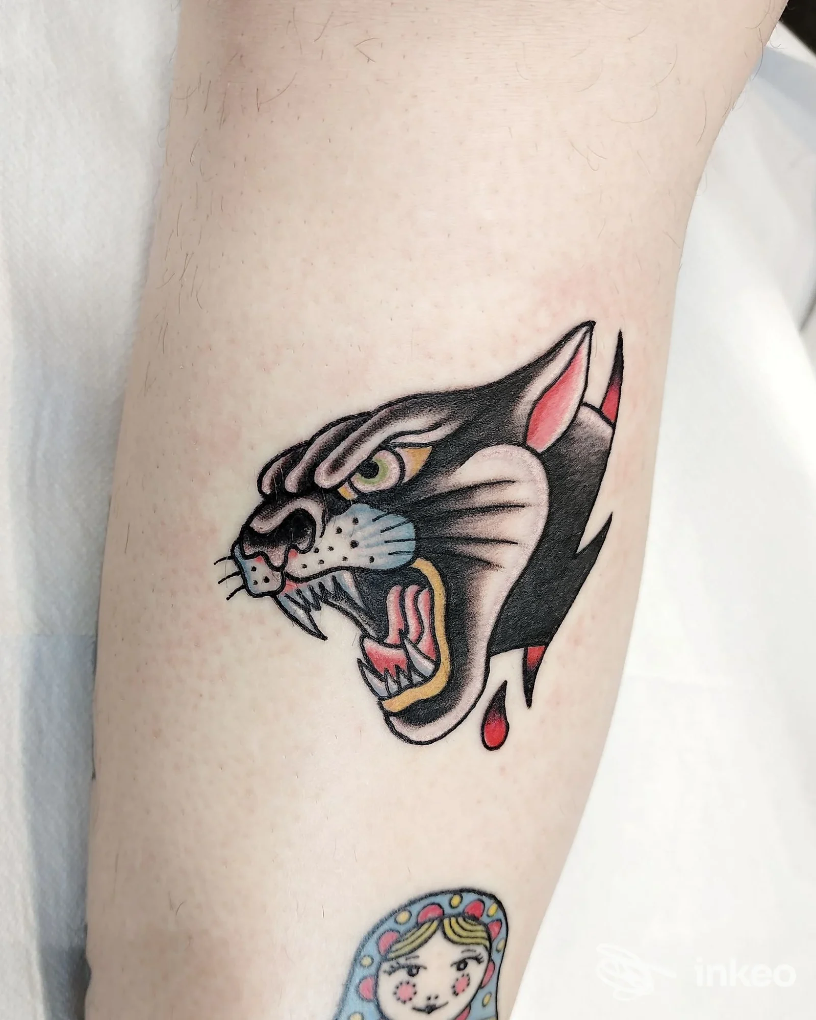 Tattoo raffigurante la testa di un gatto in stile tradizionale, sul braccio, con dettagli neri, colori vivaci e una piccola perdita di sangue simulata dalla bocca.