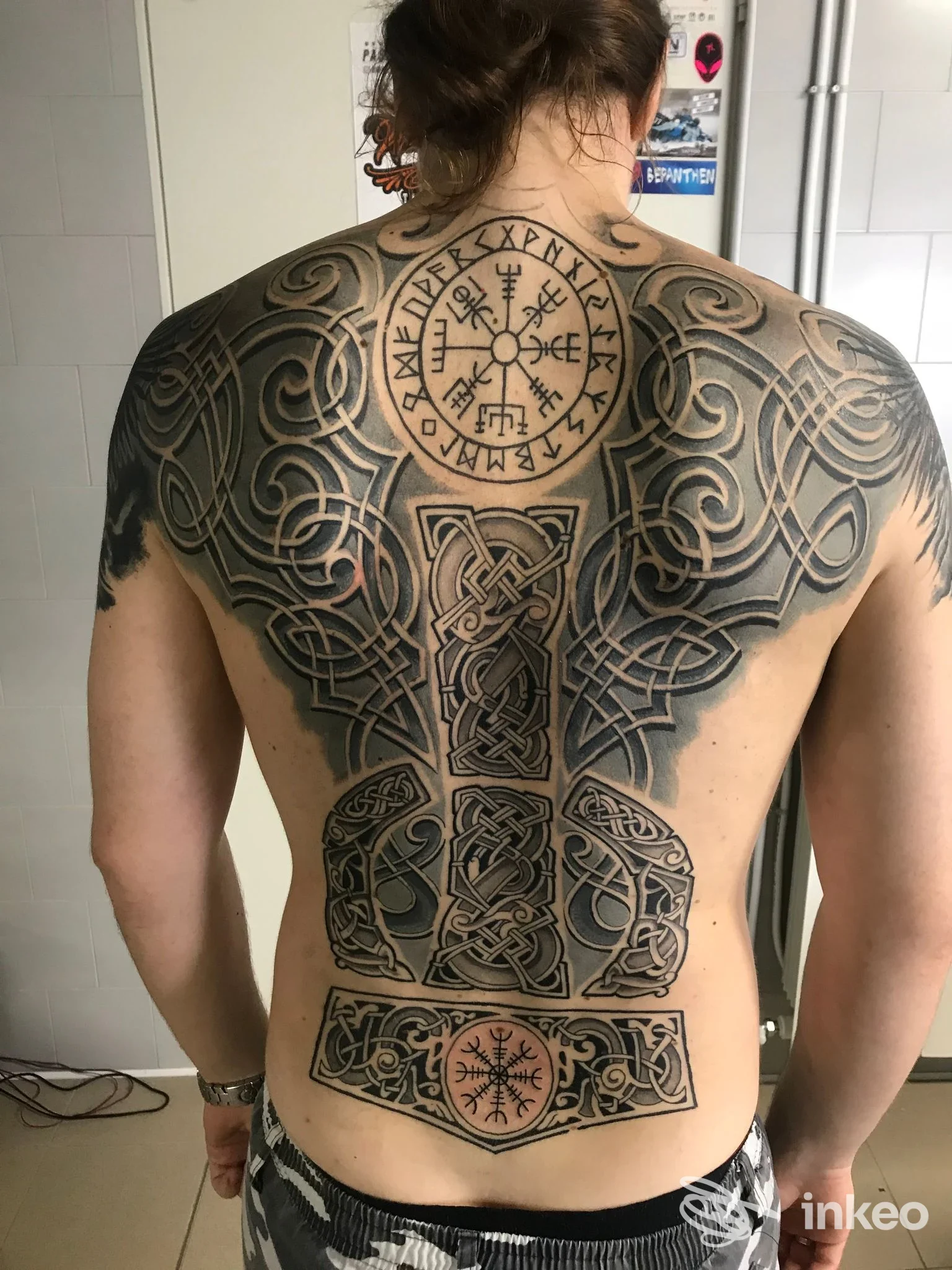 Schiena di un uomo con grande tatuaggio a motivi circolari e intrecci neri, coprente la maggior parte della schiena, visto di schiena.