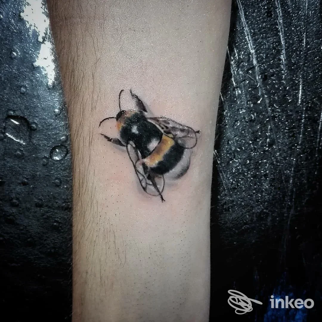 Tatuaggio realistico di un'ape sul braccio, realizzato sulla pelle, con dettagli e colori neri, gialli e bianco. Studio Remedios Tattoo.