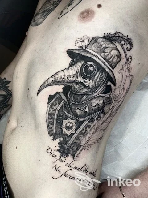 Tatuaggio in bianco e nero raffigurante un medico della peste con becco e cappello, applicato sulla pelle del torace/schiena sinistra; stile dettagliato e realisticamente eseguito, no watermark visibile.