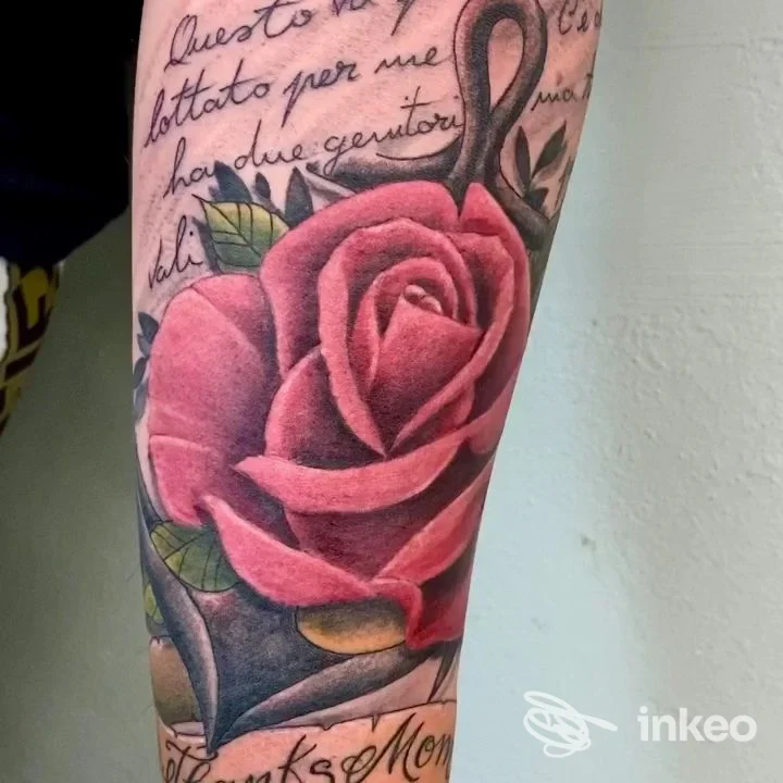 Terminale avambraccio con un grande tatuaggio realistico di rosa rosa/rossa, con scritte in corsivo lungo i margini della pelle.
