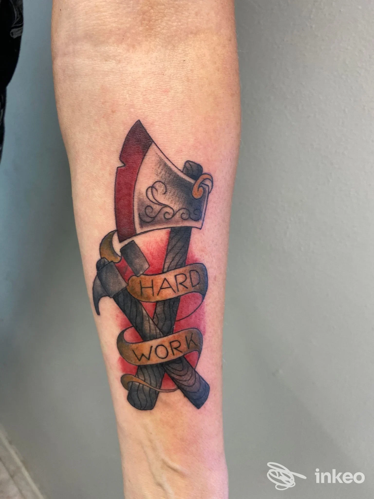 Tattoo colorato su avambraccio raffigurante una spada avvolta da nastri con parole come HARD WORK, eseguito su pelle reale.