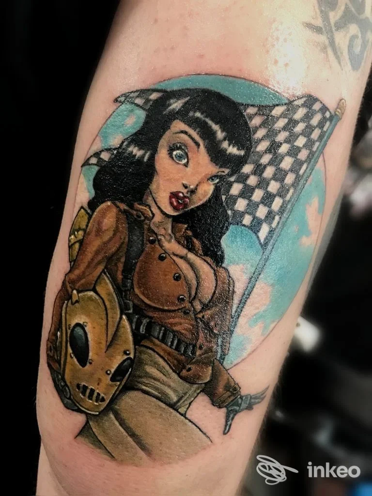 Tattoo raffigurante una giovane donna in stile cartoonesco su braccio, con capelli neri, giacca marrone e zaino, sfondo a scacchi azzurro e cerchi.