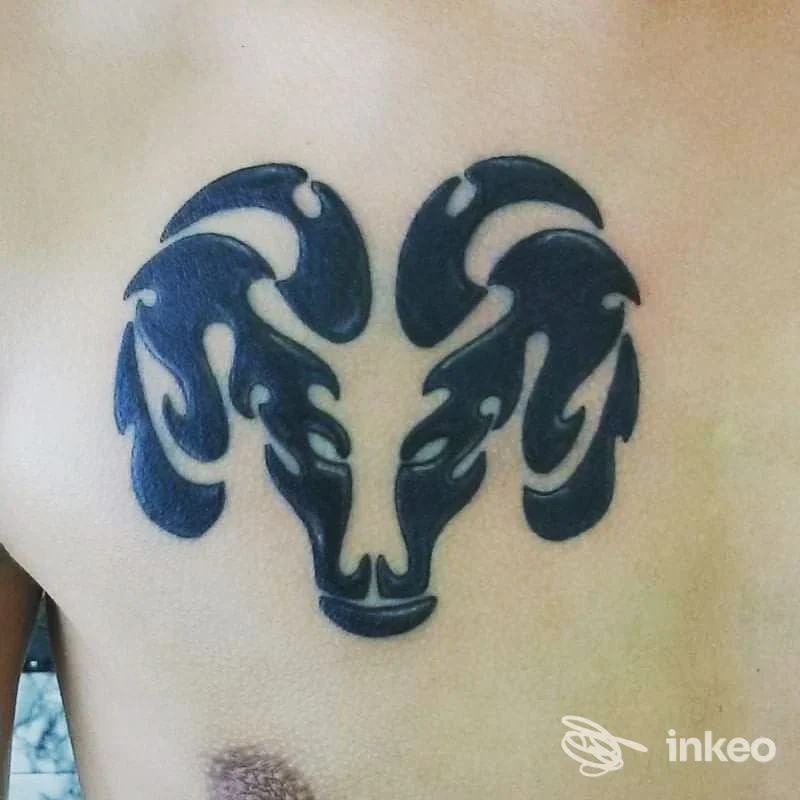 Tattoo nero su pelle raffigurante una testa di ariete stilizzata con corna prominenti sul petto.