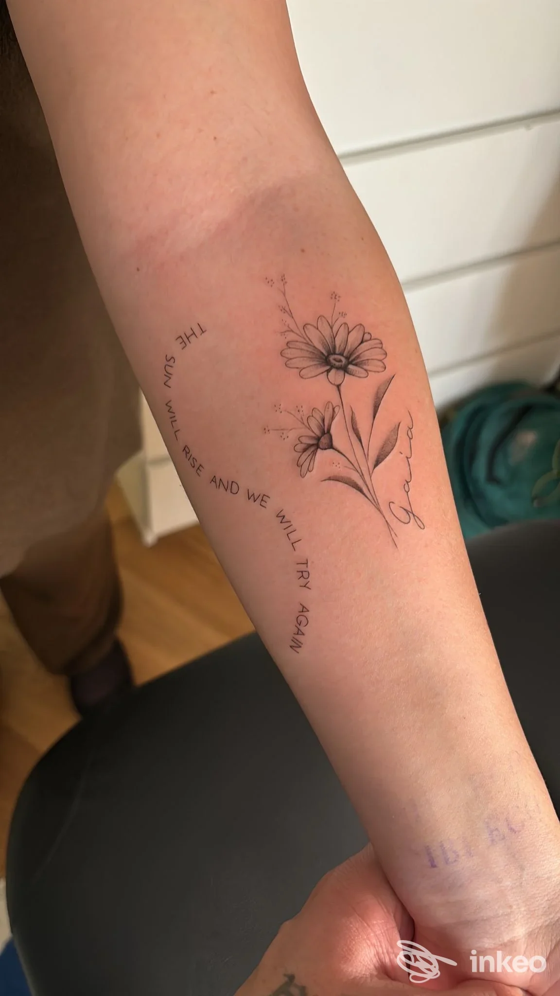 Avambraccio con fiore stilizzato in tatuaggio e testo lungo la parte interna dell’avambraccio, nessuna persona visibile, studio Hefs Fineline Tattoo.