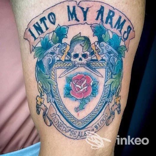 Tatuaggio a colori su pelle, braccio, con scudo, teschio e rosa al centro, senza elementi di interfaccia o overlay; aggiornato presso Ink Area Tattoo, Teramo.