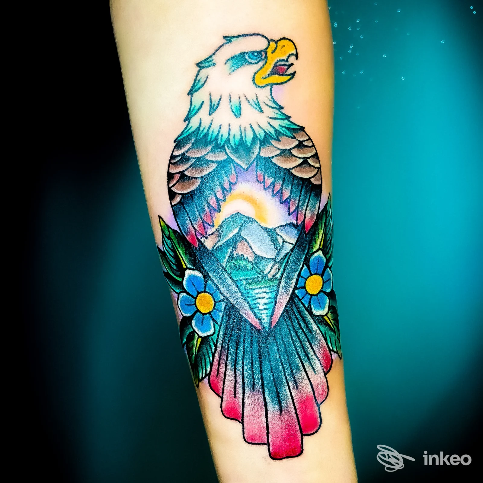 Tattoo colorato di un'aquila su braccio, con montagne e fiori, realizzato sulla pelle con linee nette e colori vividi, scatto ravvicinato su braccio. Studio Ink Area Tattoo, Teramo.