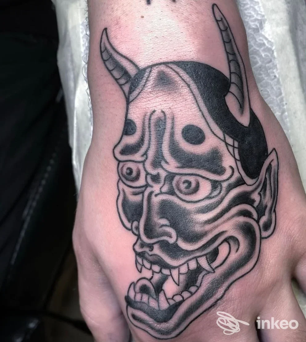 Tattoo sulla mano raffigurante un demone stilizzato con corna, linee nere e sfumature, realizzato direttamente sulla pelle.