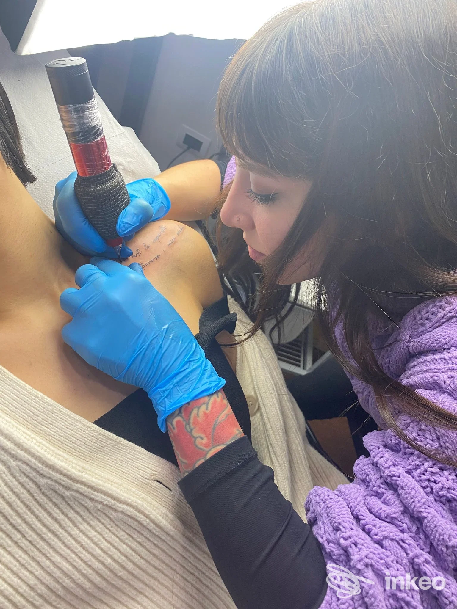 Immagine di un tatuaggio in corso: una tatuatrice con guanti blu lavora sulla pelle di una persona, con la macchina per tatuare visibile, in studio a Pescara (Stray Dog Tattoo Shop).