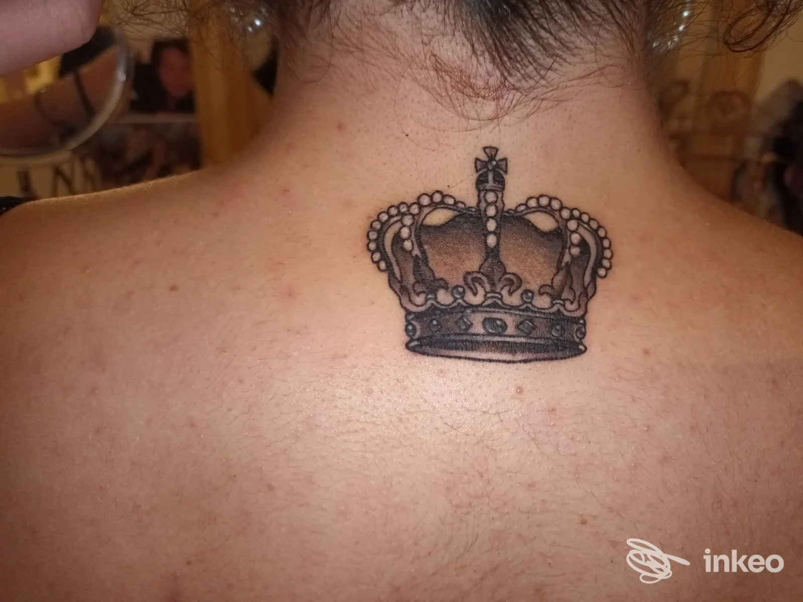 Tatuaggio reale su nuca raffigurante una corona, eseguito sulla pelle.