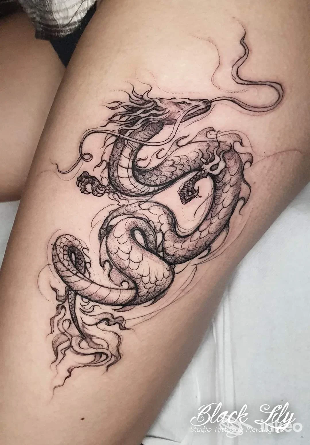 Tatuaggio su pelle raffigurante un drago-serpente in stile linework nero, visibile sulla gamba/coscia.