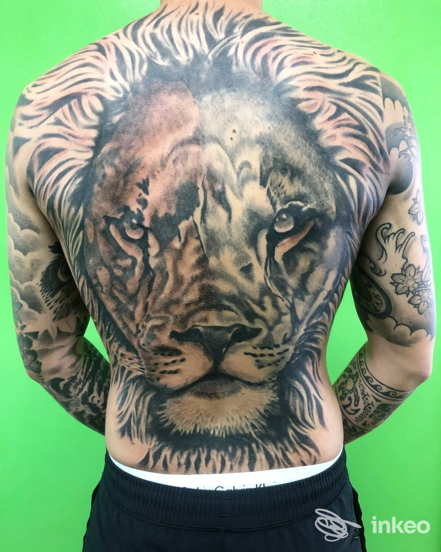 Schiena di uomo con tatuaggio realistico a tema tigre, dettagliata resa del muso e degli occhi, sfondo verde acceso.