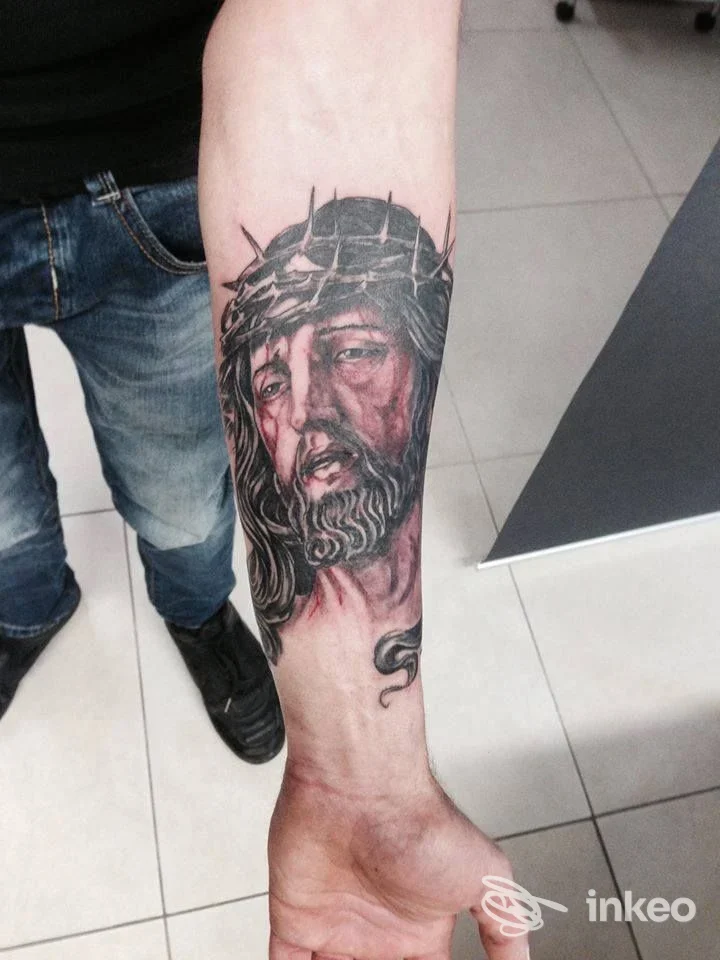 Tattoo realistico sull’avambraccio raffigurante Gesù con corona di spine, eseguito su pelle reale, indossa jeans: foto in studio Tattoo Village, Colonnella.