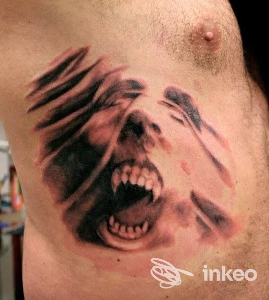 Tattoo realistico su braccio raffigurante una figura urlante con dettagli neri e rossi, visibile solo una parte del corpo.