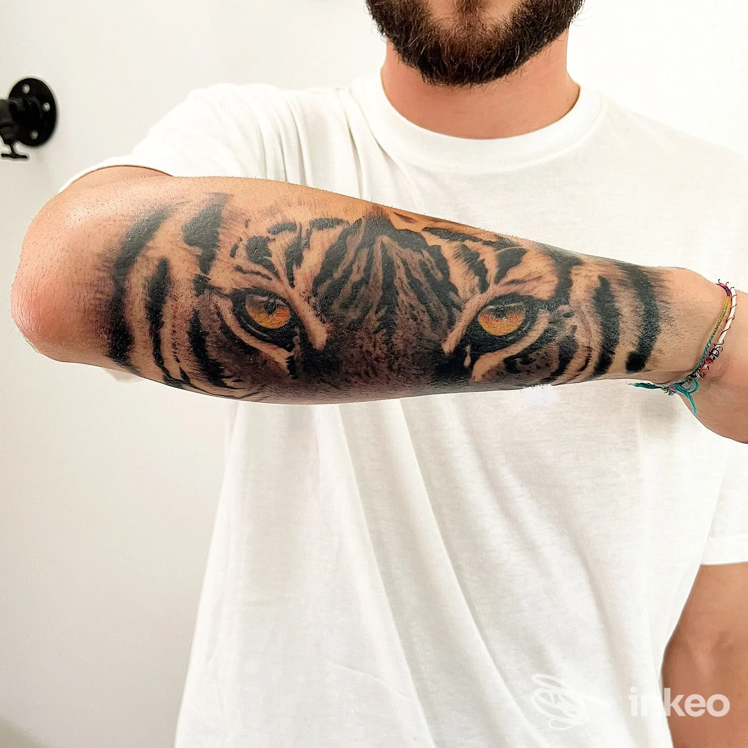 Tatoueur portant un tattoo réaliste d’un tigre sur l’avant-bras, regard intense des yeux du tigre, peau visible et tatouage sombre sur chemise blanche, ambiance neutre.