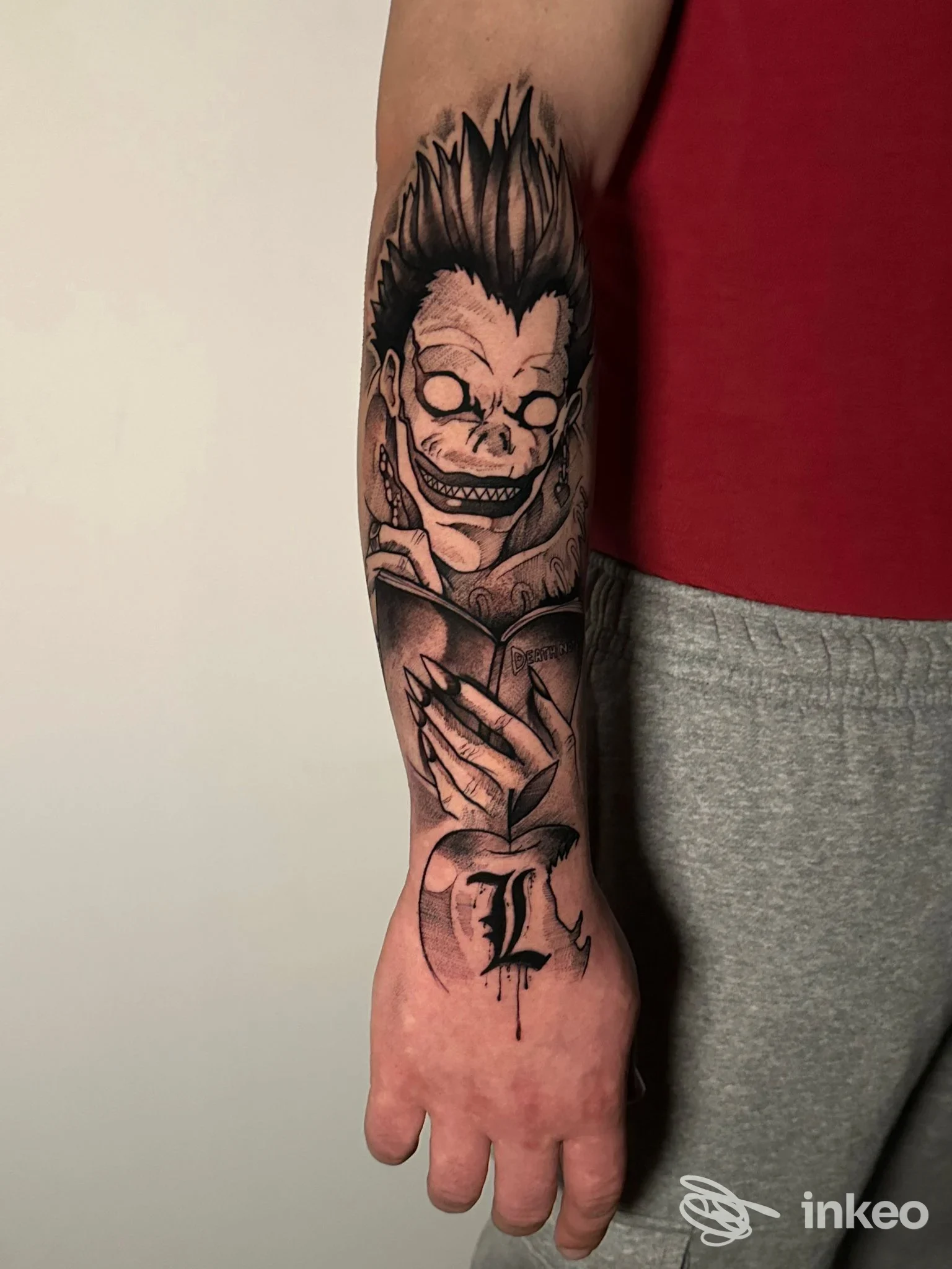 Avambraccio di una persona con tatuaggio in stile manga raffigurante un personaggio sorridente e dai tratti scuri, linee nette e shading marcato.