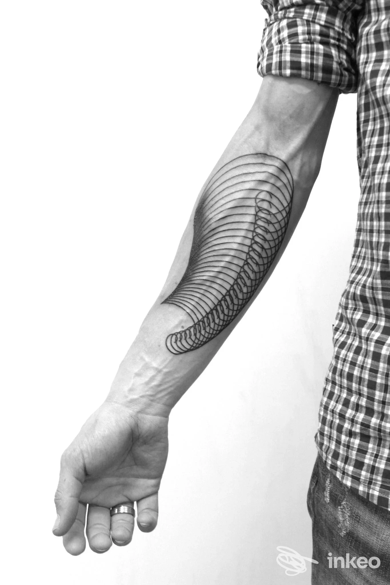 Avambraccio di uomo con tatuaggio geometrico a linee curve, in bianco e nero, visibile su pelle reale.