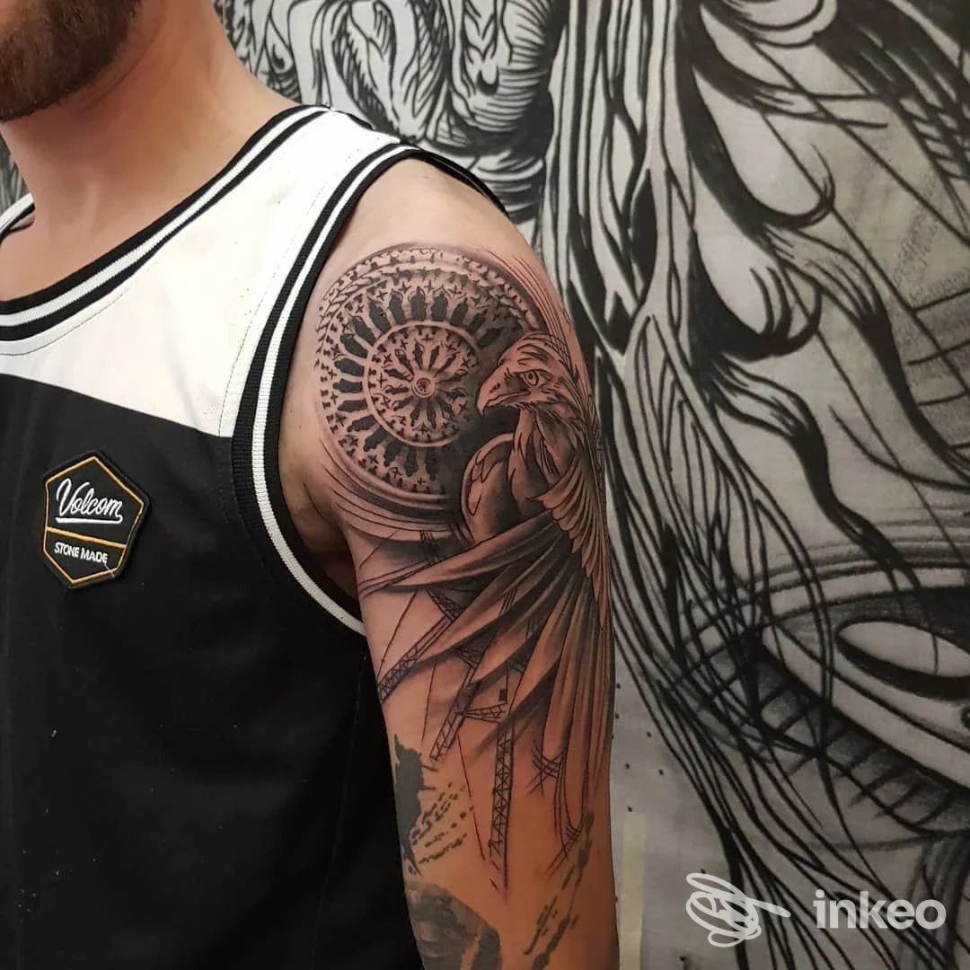 Tattoo sul braccio raffigurante un motivo circolare serrato vicino a una figura di uccello, realizzato sulla pelle del braccio, con sfondo decorativo.