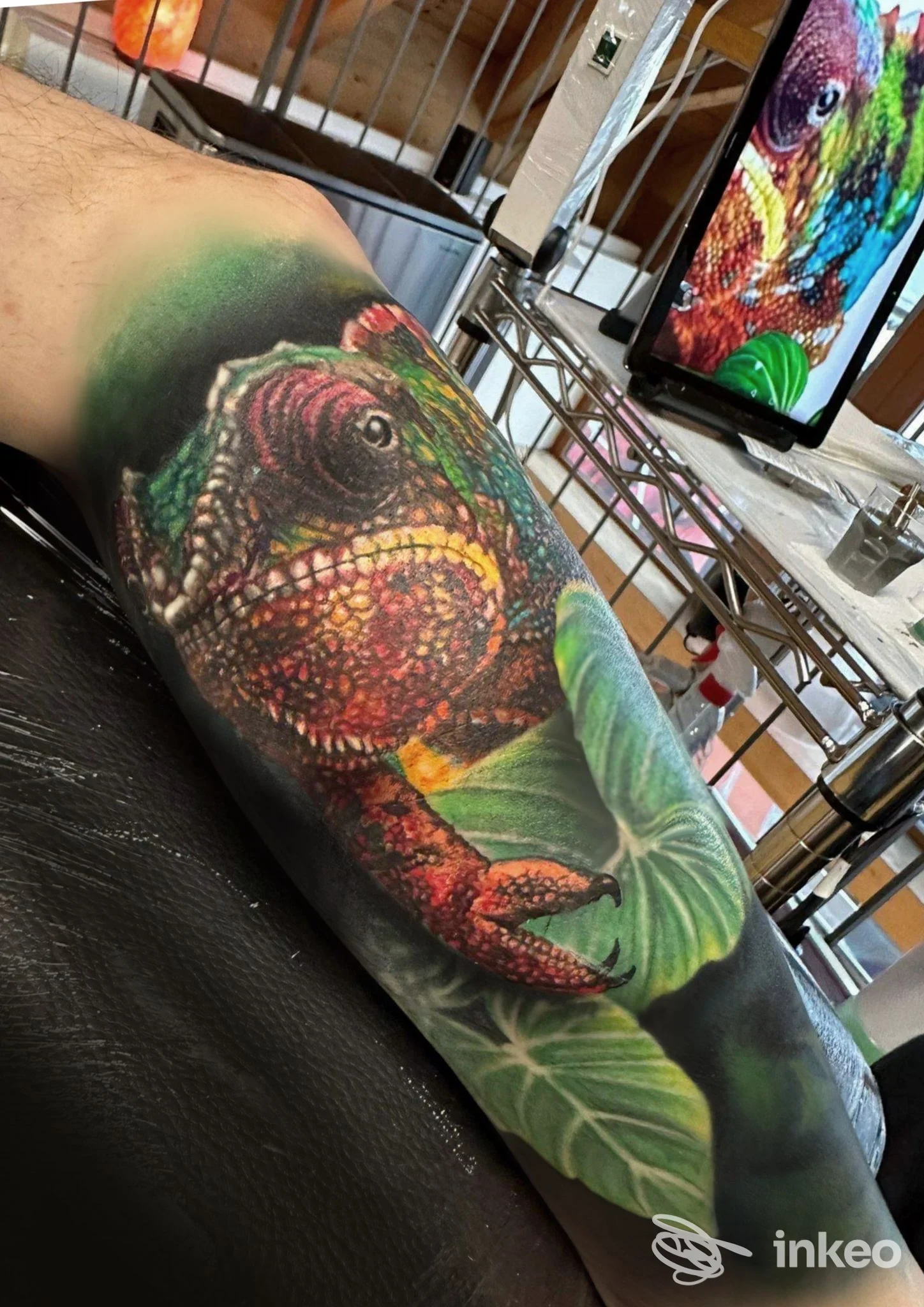 Tatuaggio colorato su avambraccio raffigurante un dinosauro con foglie, realizzato direttamente sulla pelle in un contesto di studio tattoo.