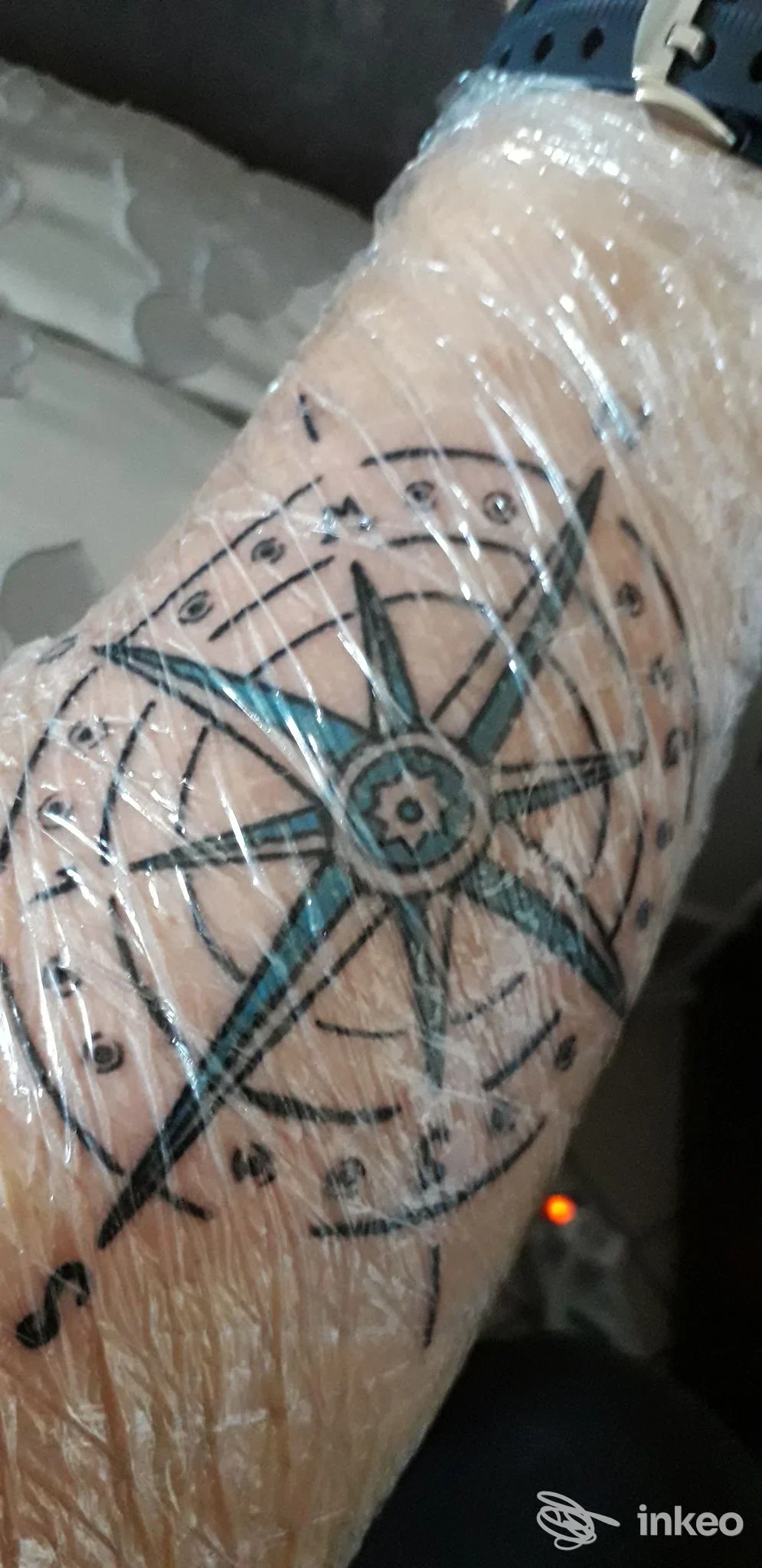 Tatuaggio visibile sul braccio raffigurante un motivo geometrico a stella/compasso con contorni neri e riempimenti azzurri, avvolto in pellicola; studio Crazy Pin Up Tattoo, Sant'Egidio alla Vibrata.